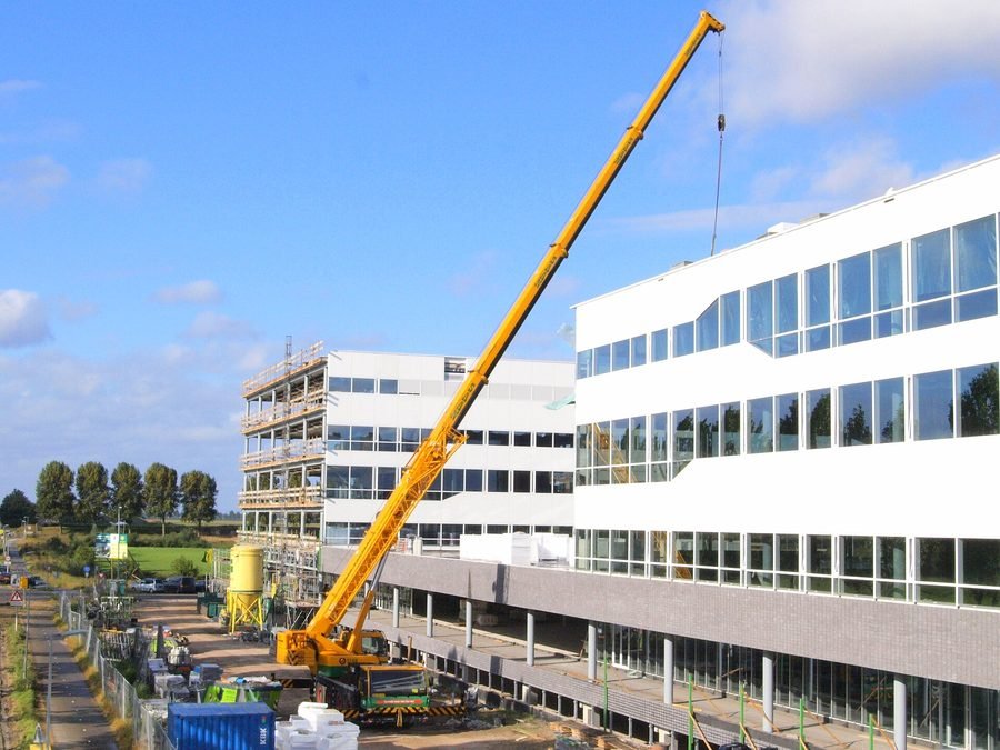 Grue mobile en levage, flèche déployée au-dessus d'un immeuble de bureaux
