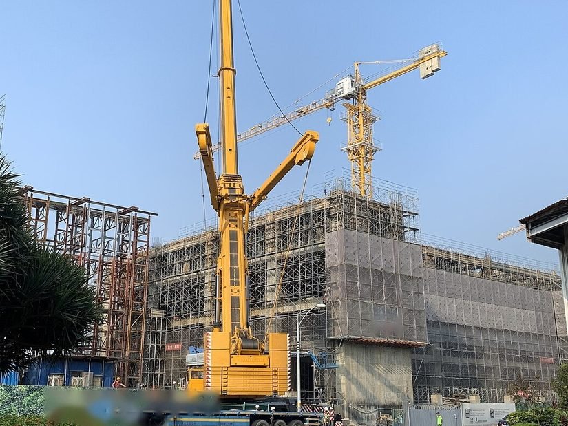 Grue mobile de grande capacité, flèche dressée devant un bâtiment en construction